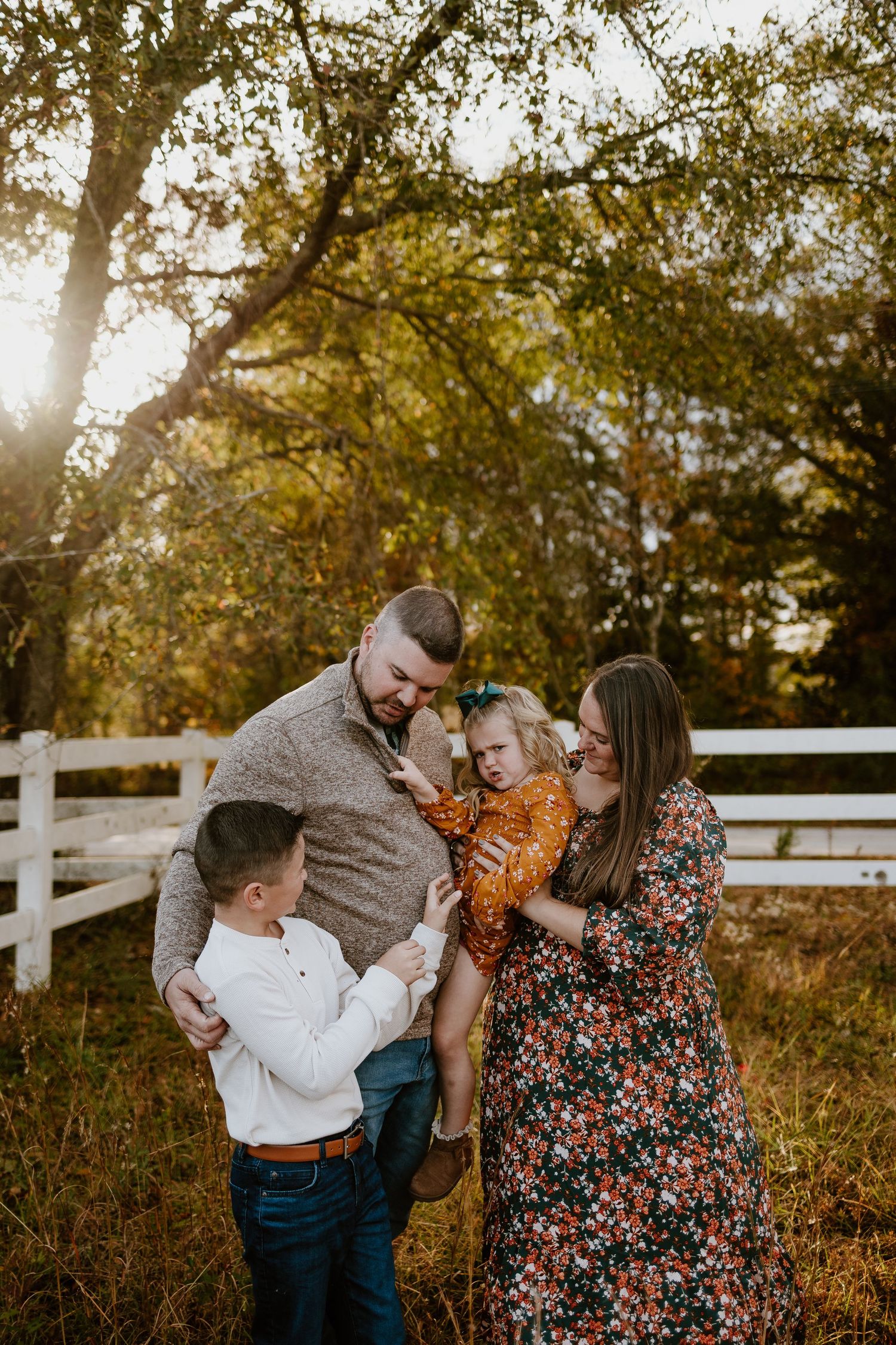 Happy family of four sharing a joyful moment outdoors near white fence during golden hour.