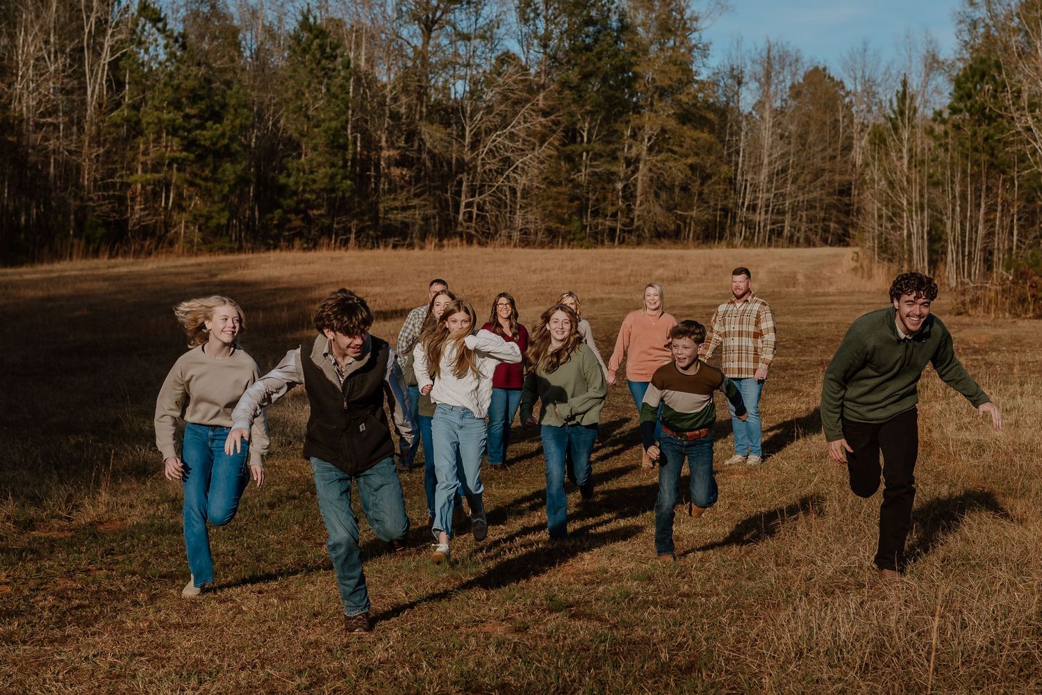 Large group of people joyfully running together across an open field with trees in background.