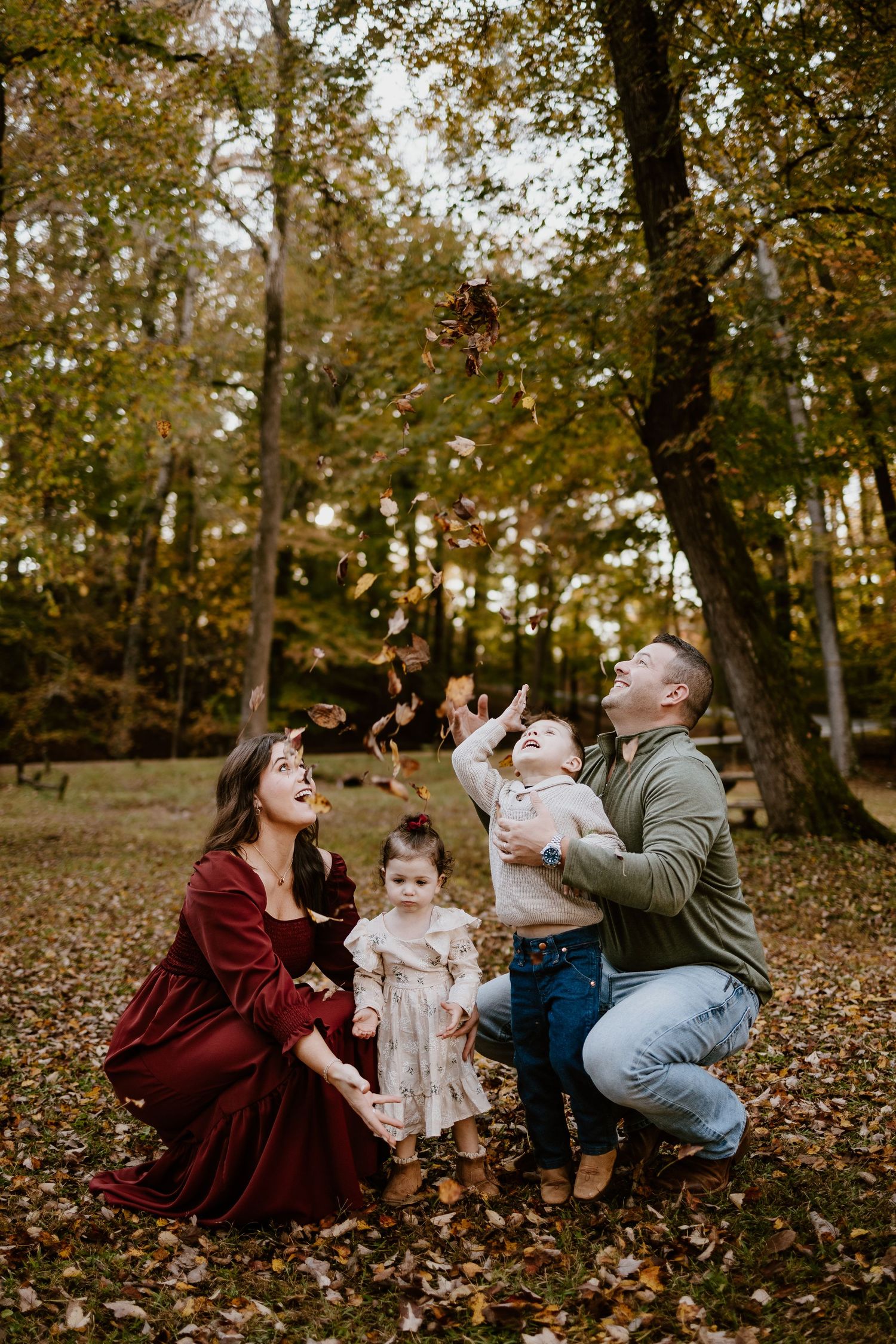 Joyful family of four tosses autumn leaves in a colorful fall park setting at golden hour.