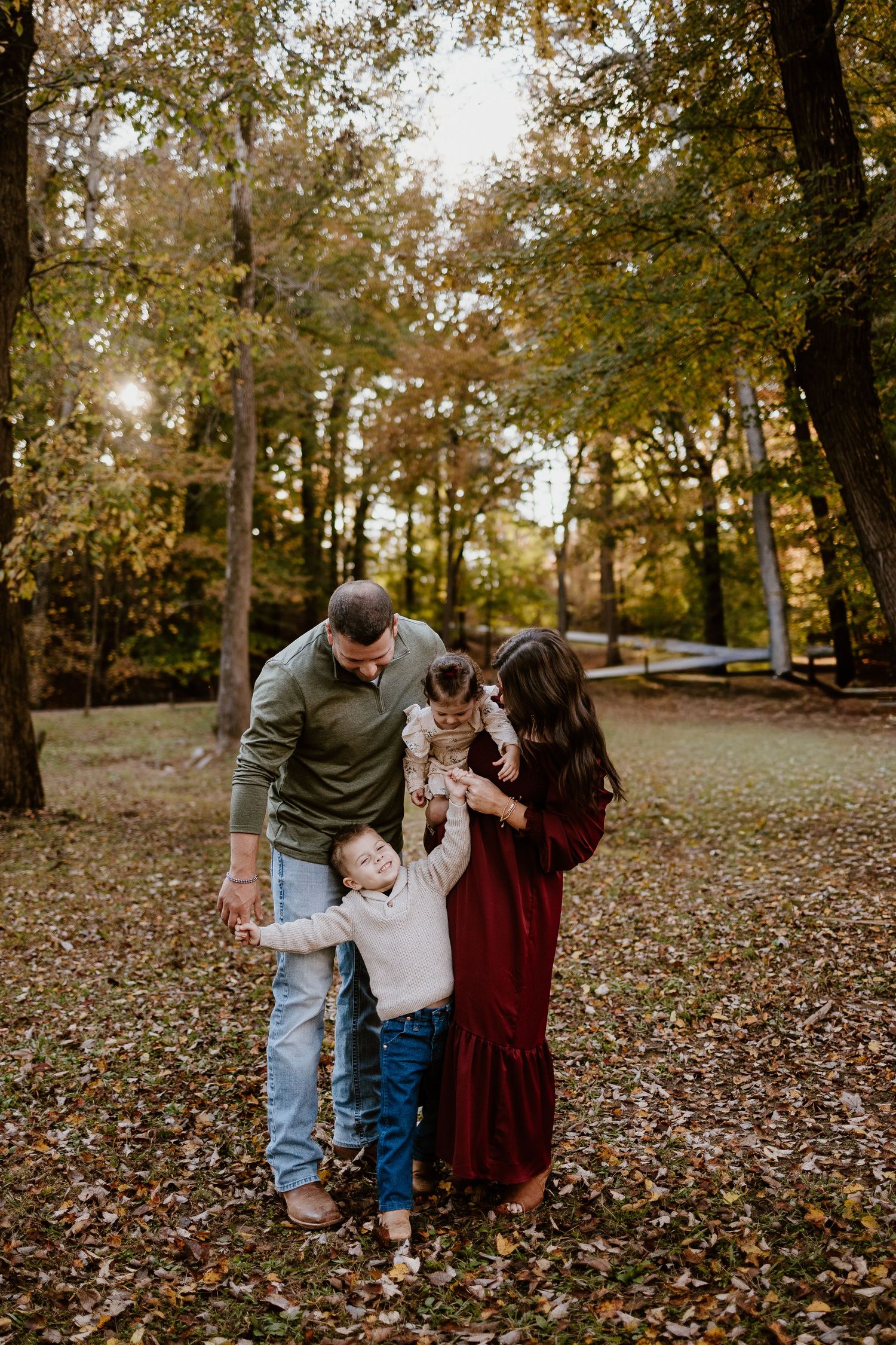 Family of four shares a joyful moment among colorful autumn leaves in a sunlit woodland park.