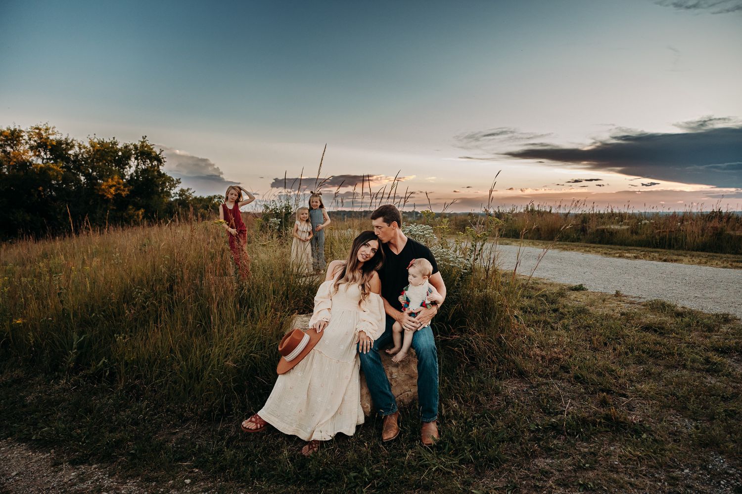 A family poses together at golden hour along a rural dirt road surrounded by tall grass.