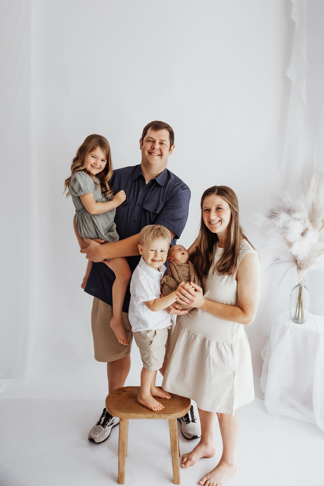 Happy family of five with newborn posing in bright white studio.