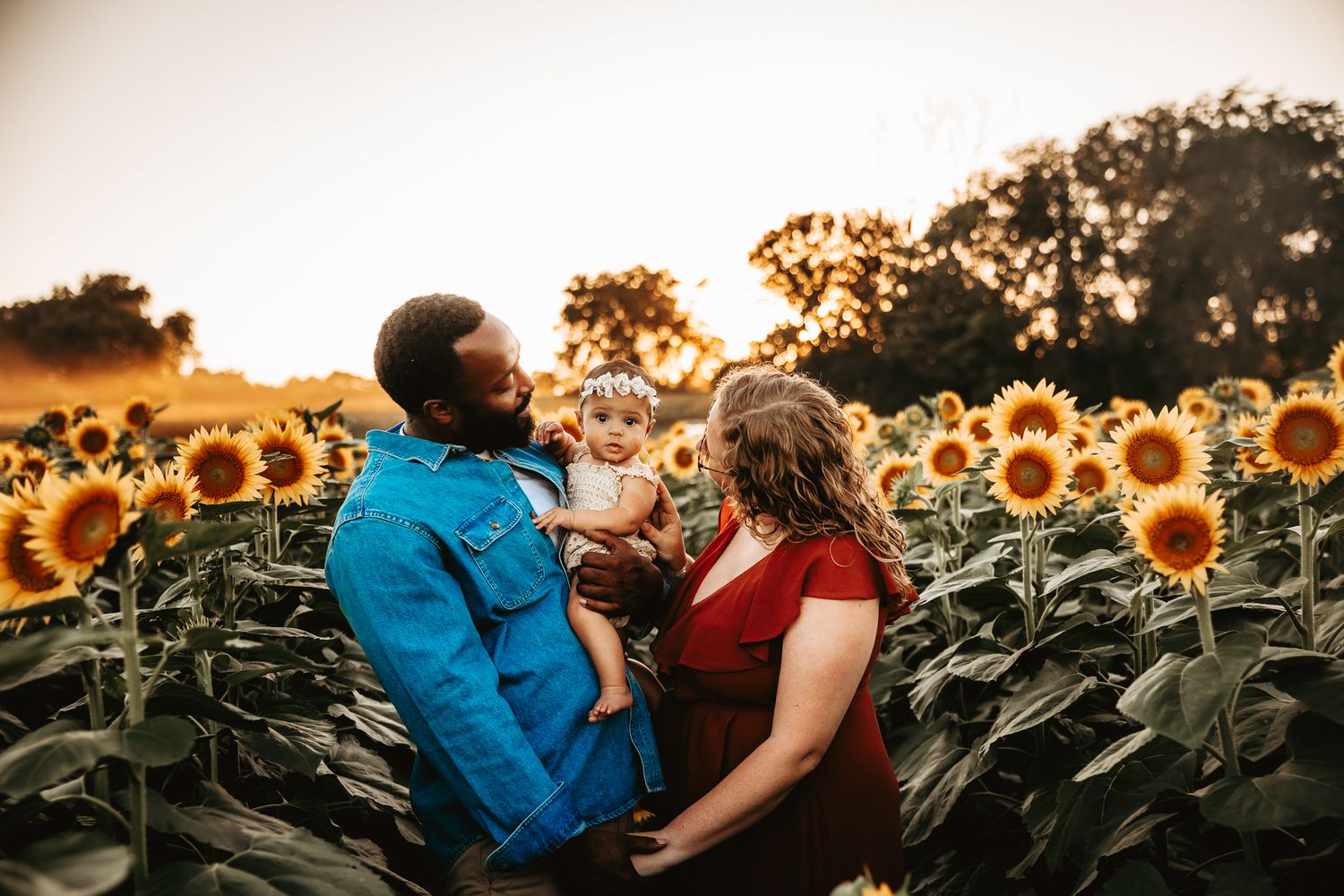 A joyful interracial family shares a warm moment together in a vibrant sunflower field at sunset.