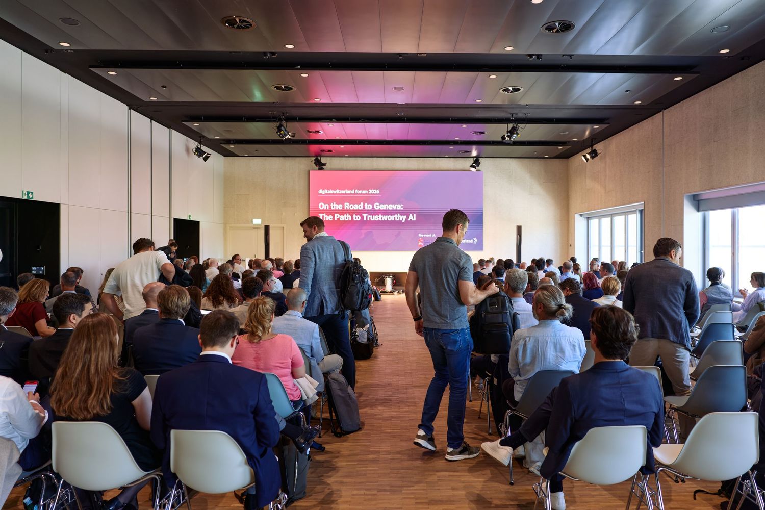 Group of people in a conference room facing a large screen displaying “digitalswitzerland Forum 2026: The Path to Trustworthy AI.”