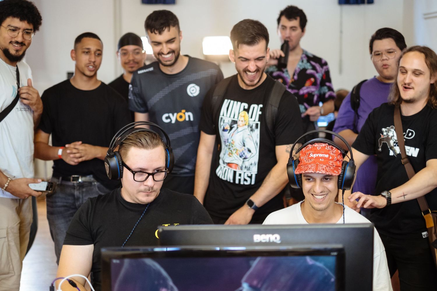 Group of gamers gathered around a BenQ monitor at an esports event, smiling and wearing headphones.