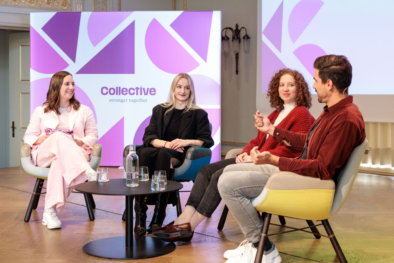 Four professionals engage in a panel discussion at a Collective Gathering event, seated in modern chairs on a stage.