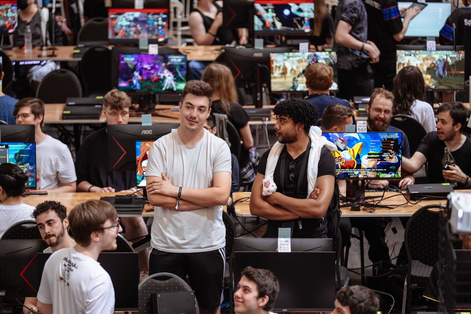 Gamers socializing at a large esports gaming event with multiple PC setups and colorful monitors in the background.