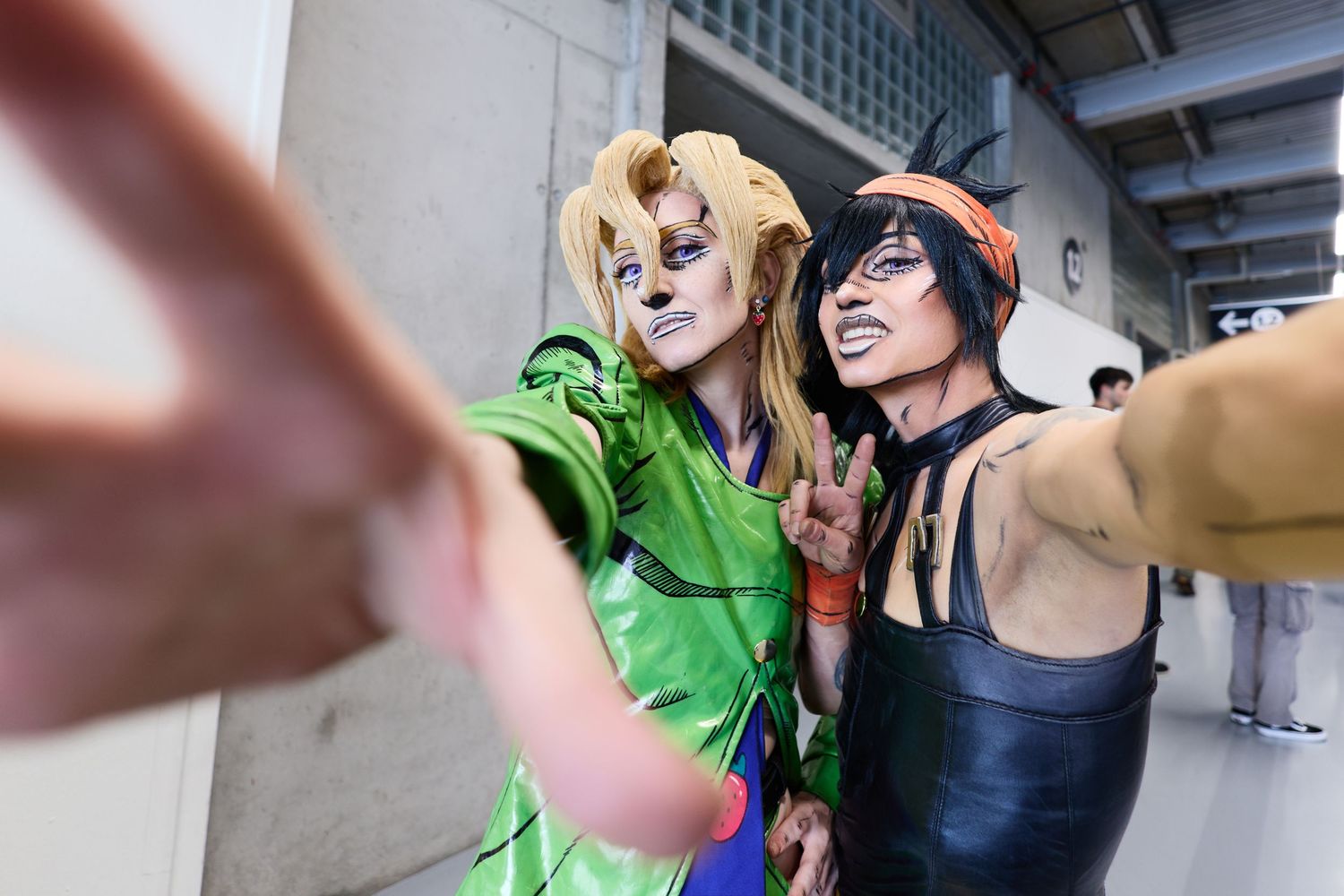 Two people in detailed JoJo's Bizarre Adventure cosplay as Giorno Giovanna and Narancia Ghirga pose with expressive makeup and hand gestures