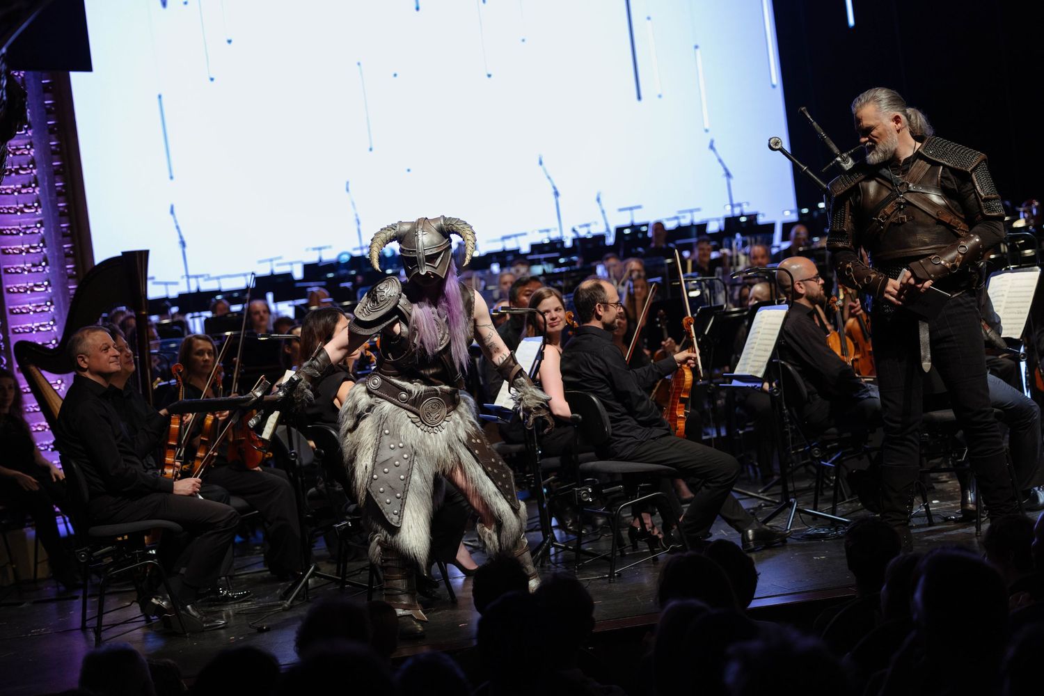 Costumed performer in dragon armor interacts with orchestra musicians on stage during a live gaming-themed concert.