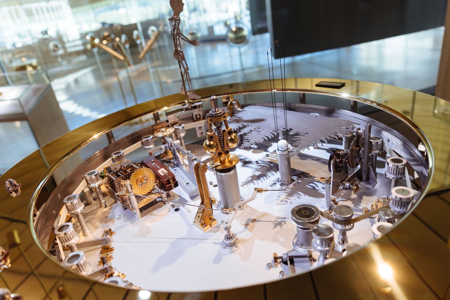 Close-up of an intricate precision mechanical clock movement on a polished silver base in a museum display.