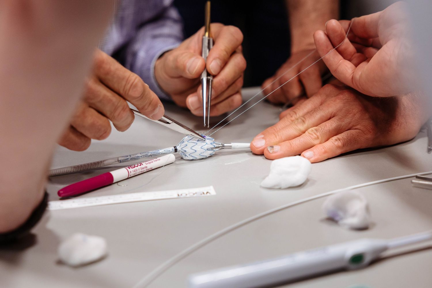 Hands-on demonstration of a vascular medical device, with clinicians using surgical tools to manipulate a stent-like device on a table.