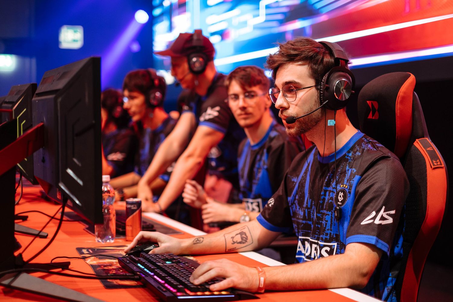 Esports players competing at gaming stations with monitors during a professional tournament event.