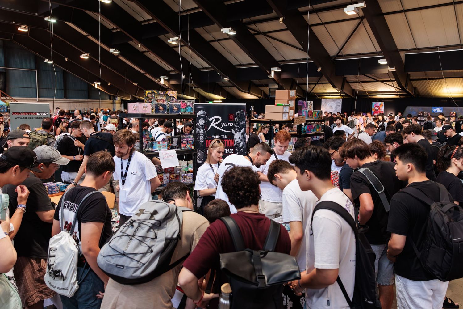 Large crowd of people browsing vendors at the Schweizer Sammelkartenmesse, an indoor trading card show.