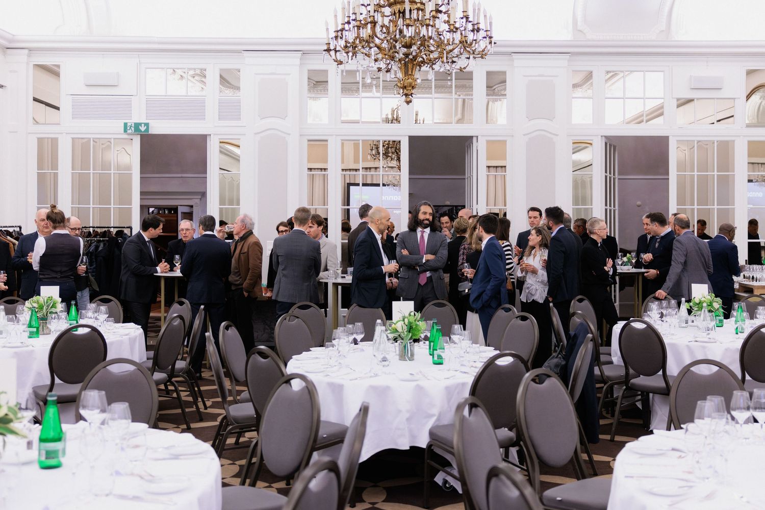 Elegant banquet hall with round white-clothed tables, chandelier, and formally dressed guests mingling at a networking event.