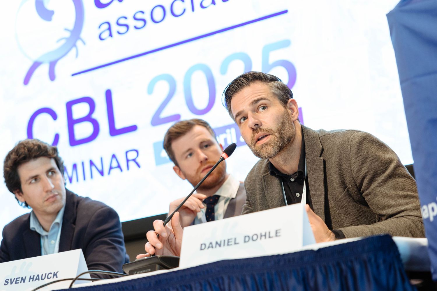 Daniel Dohle and Sven Hauck speak at CBL 2025 Seminar panel discussion with microphones on table.