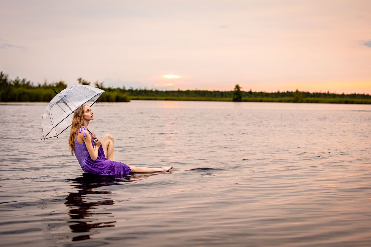 Creative portrait of a woman in a purple dress sitting in the water at sunset