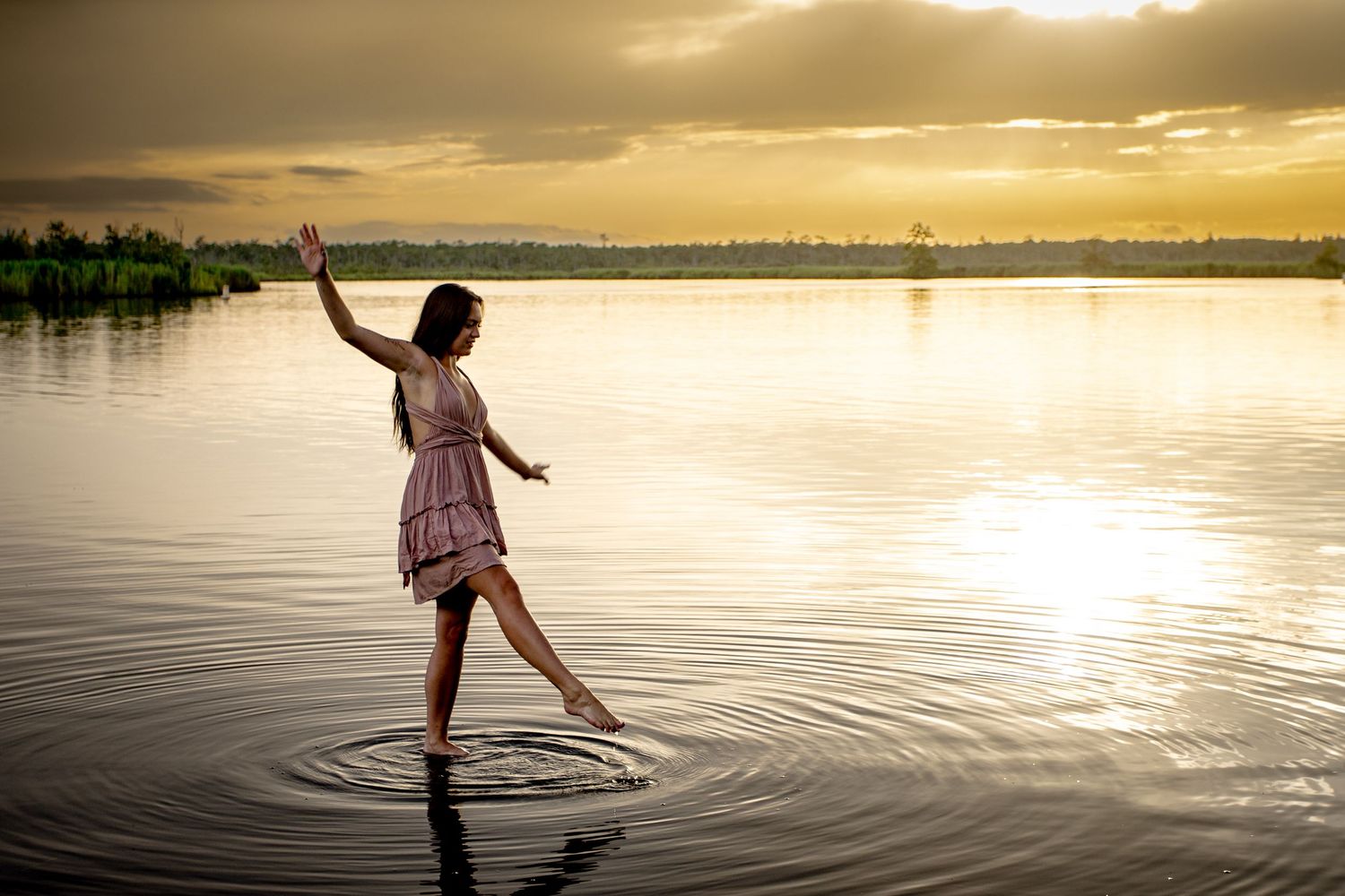 Creative portrait of a woman walking through shallow water at sunset—
