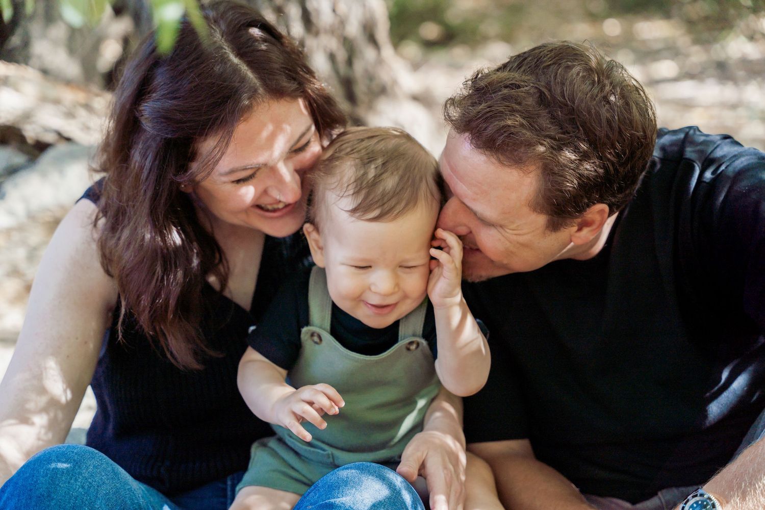 Parents kissing and cuddling their baby boy outdoors in nature.