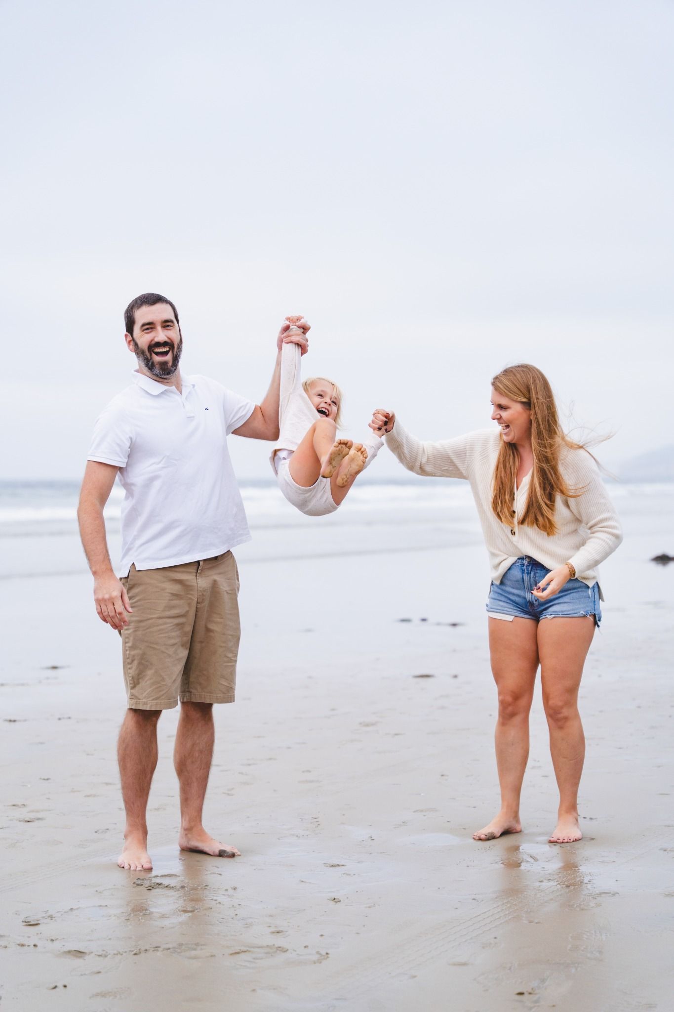 Happy family swinging young child between them on a sandy beach, smiling and enjoying a fun day by the ocean.