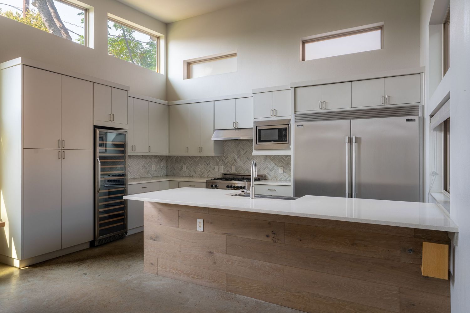Modern kitchen with stainless steel appliances, white cabinetry, marble backsplash, large island, and wine cooler.