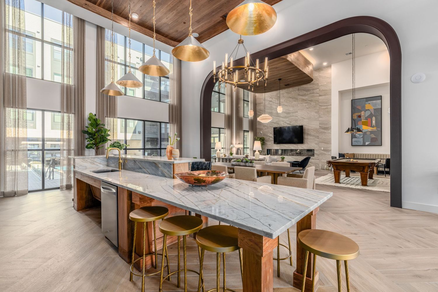 Luxurious open-concept kitchen with marble island, gold bar stools, pendant lights, and elegant arched entryway to living area.
