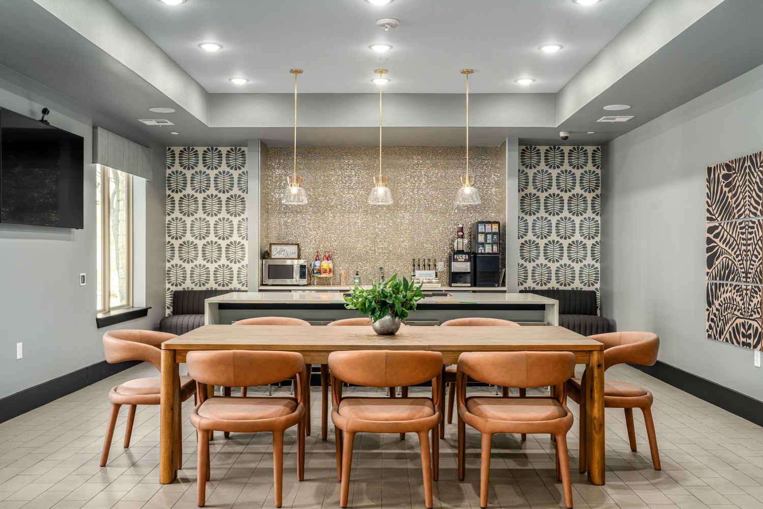 Modern dining area with leather chairs, wooden table, pendant lights, and stylish geometric wallpaper in a hotel lounge.