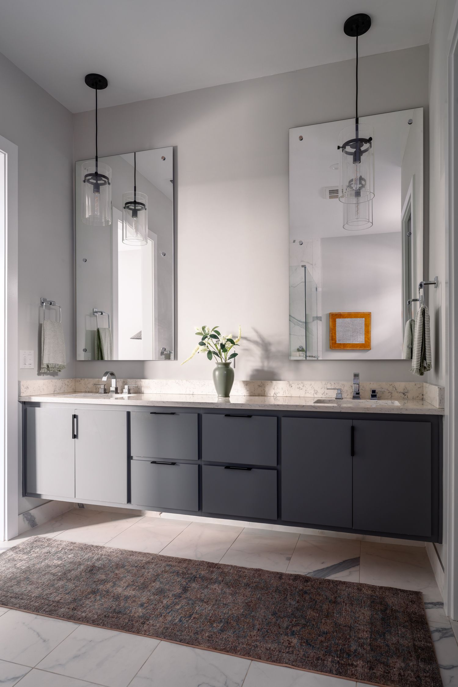 Modern double vanity bathroom with dark gray floating cabinets, dual pendant lights, tall mirrors, and marble countertops.