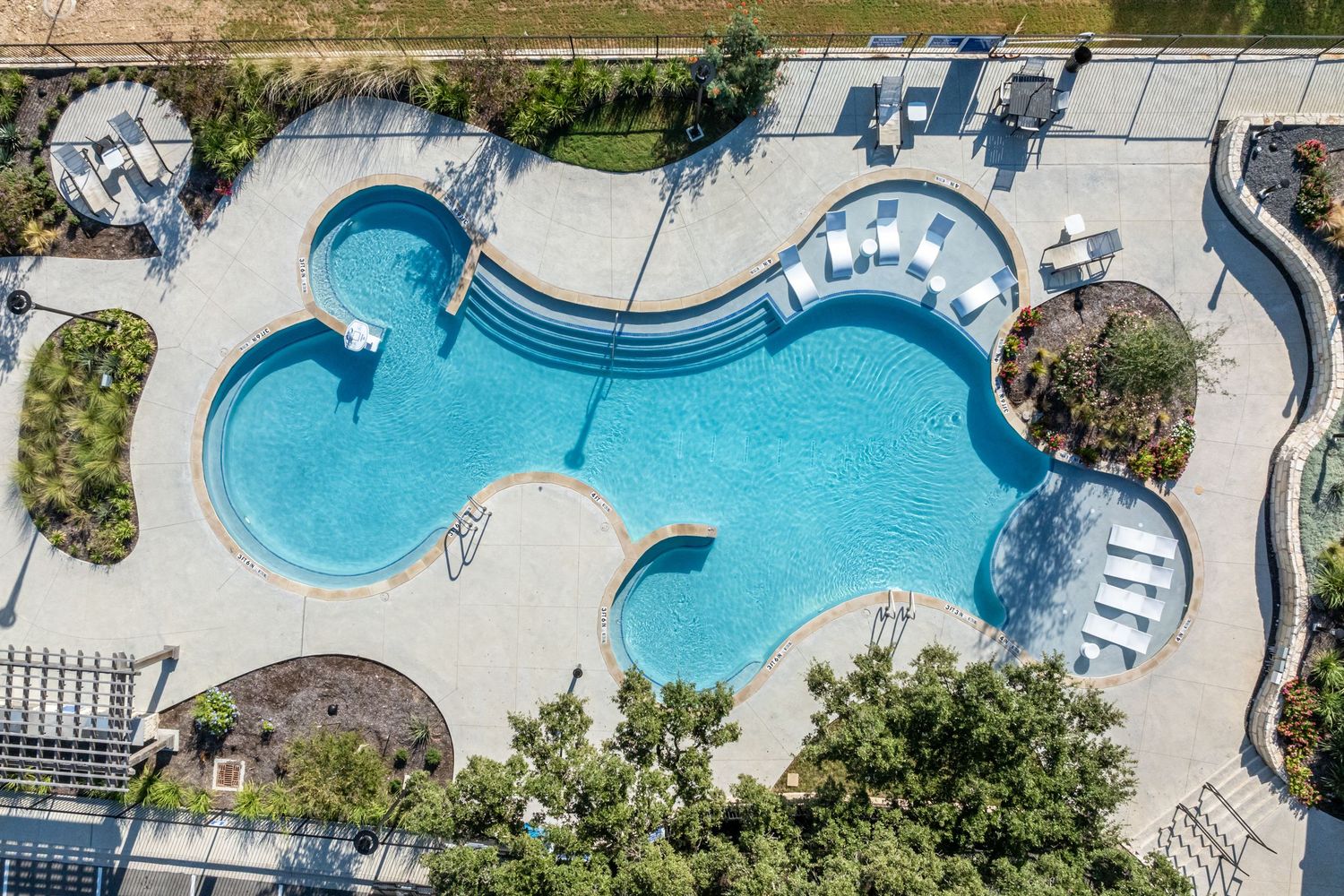 Aerial view of a freeform swimming pool with blue water, lounge chairs, and landscaping at a resort.