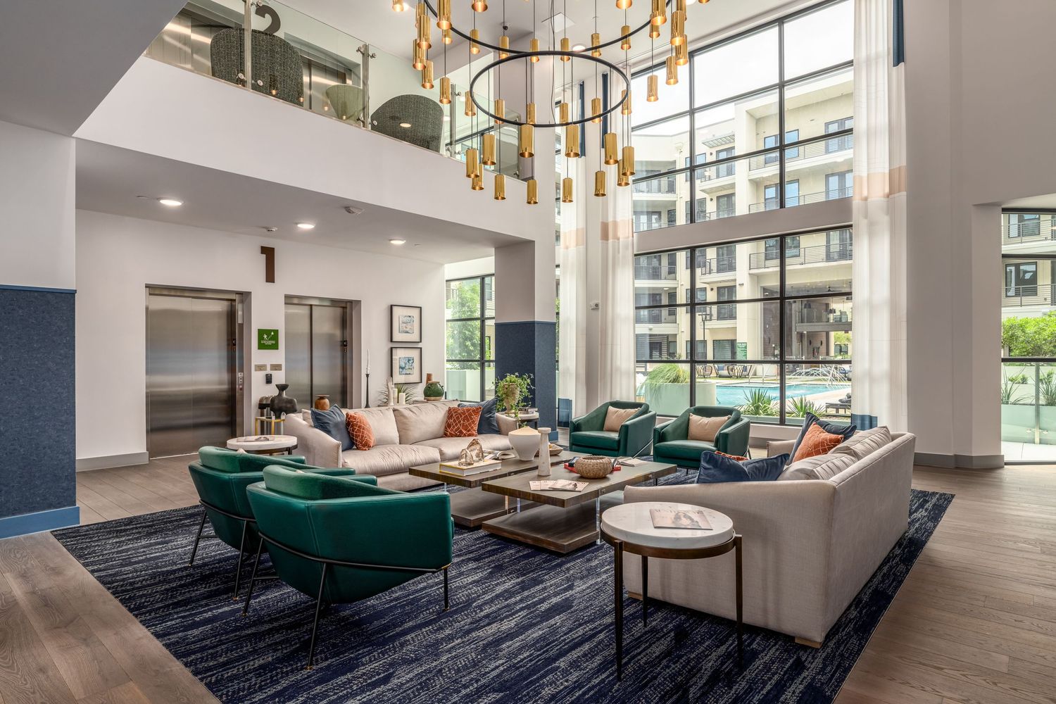 Modern luxury apartment lobby with teal chairs, gray sofas, gold chandelier, and floor-to-ceiling windows.
