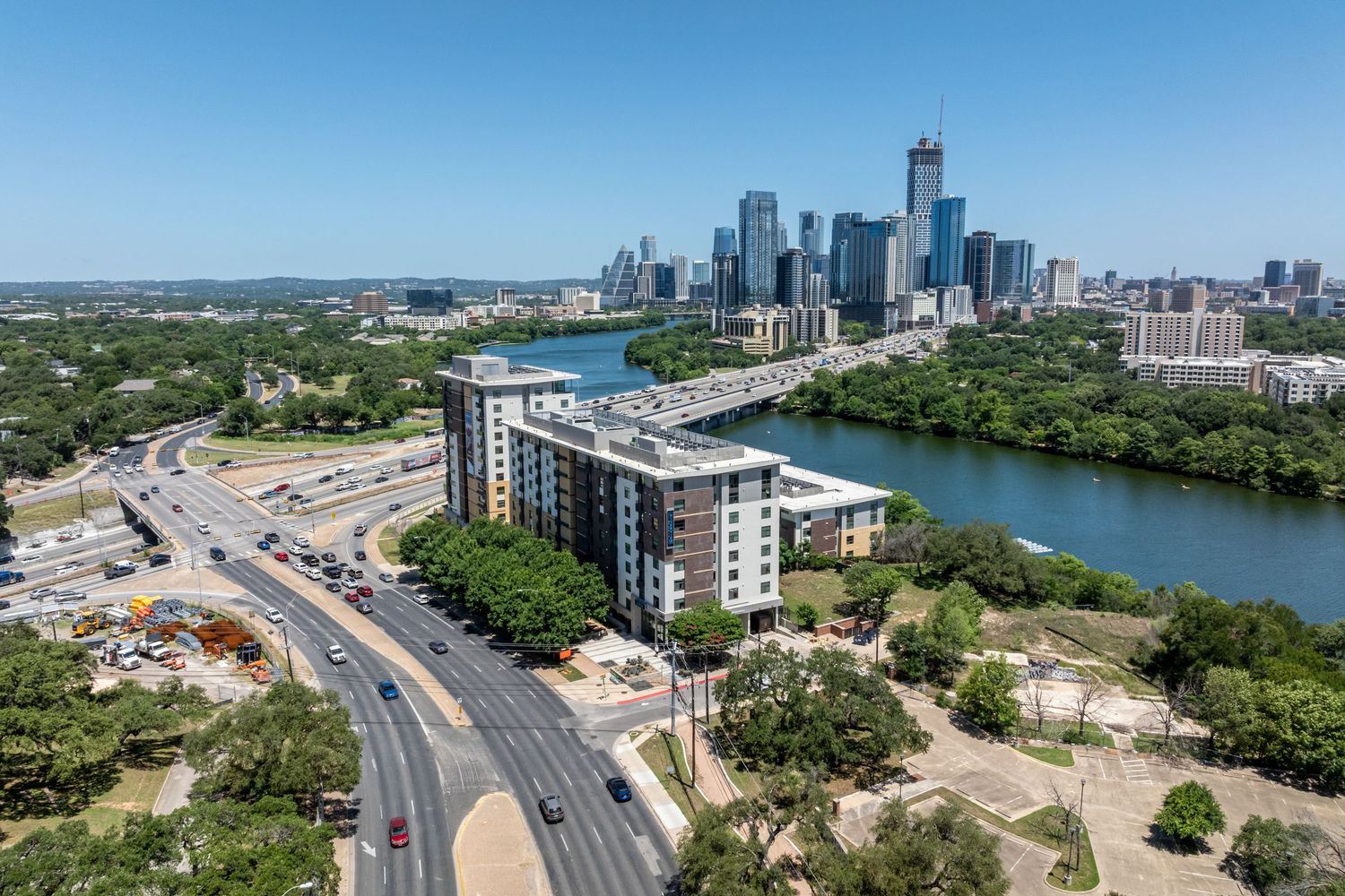 Aerial view of Austin Texas skyline along Lady Bird Lake with modern apartment complex and busy highway interchange.