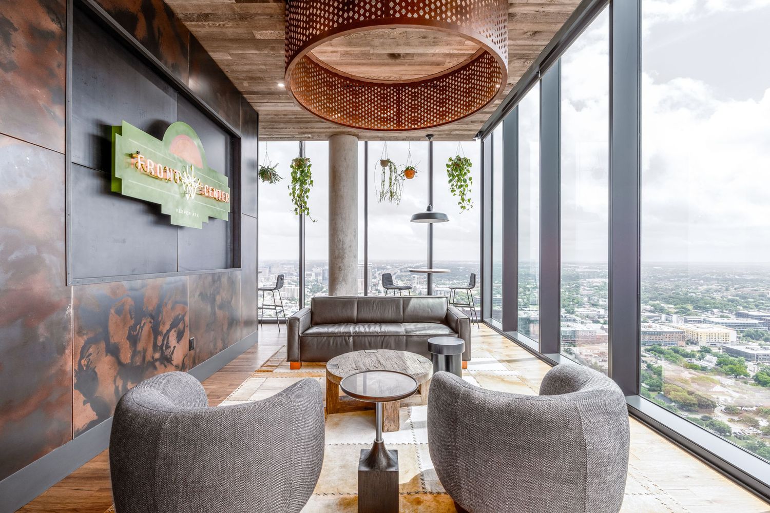 Modern high-rise lounge with gray curved chairs, copper accents, pendant light, and floor-to-ceiling windows overlooking city views.
