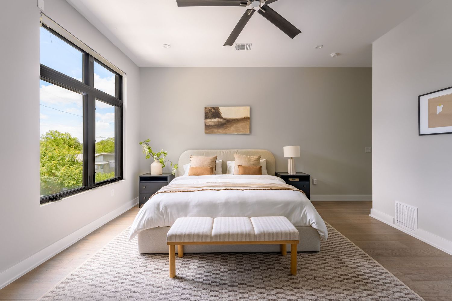 Modern bedroom with gray walls, large windows, hardwood floors, white bedding, and a ceiling fan.