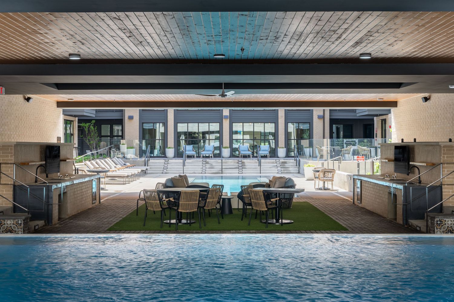 Luxury resort pool area with outdoor seating, dining tables, and a spacious clubhouse with large windows.