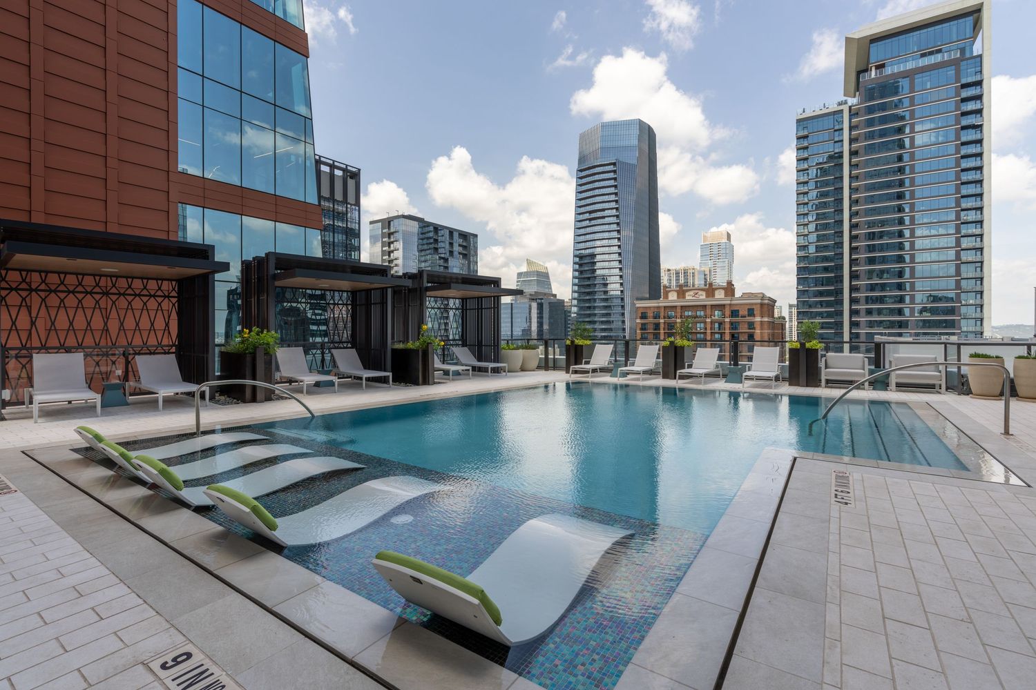 Rooftop pool with lounge chairs overlooking a modern city skyline on a sunny day.