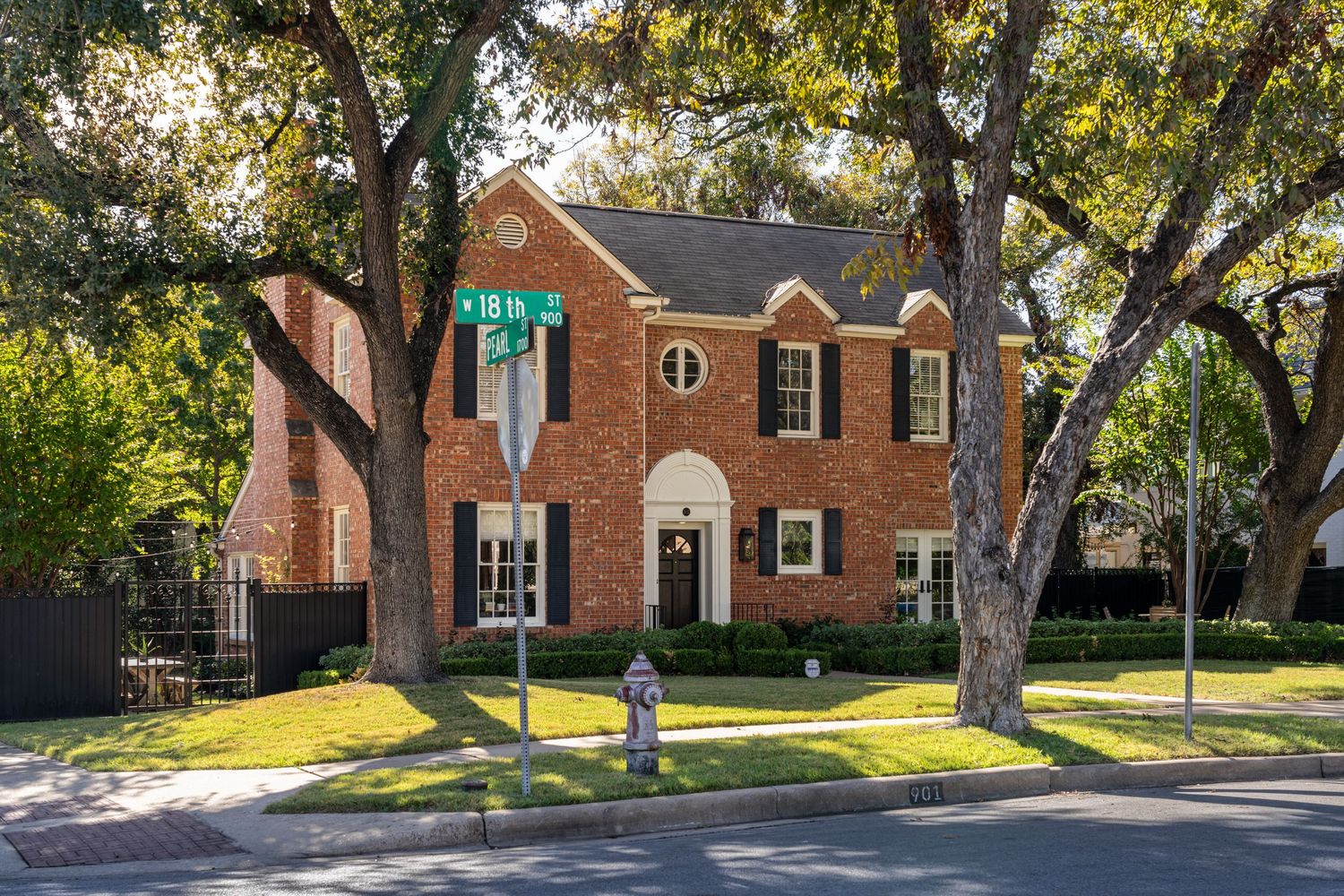 Elegant two-story brick Colonial home on a tree-lined corner lot with lush green lawn and classic white-trimmed windows.