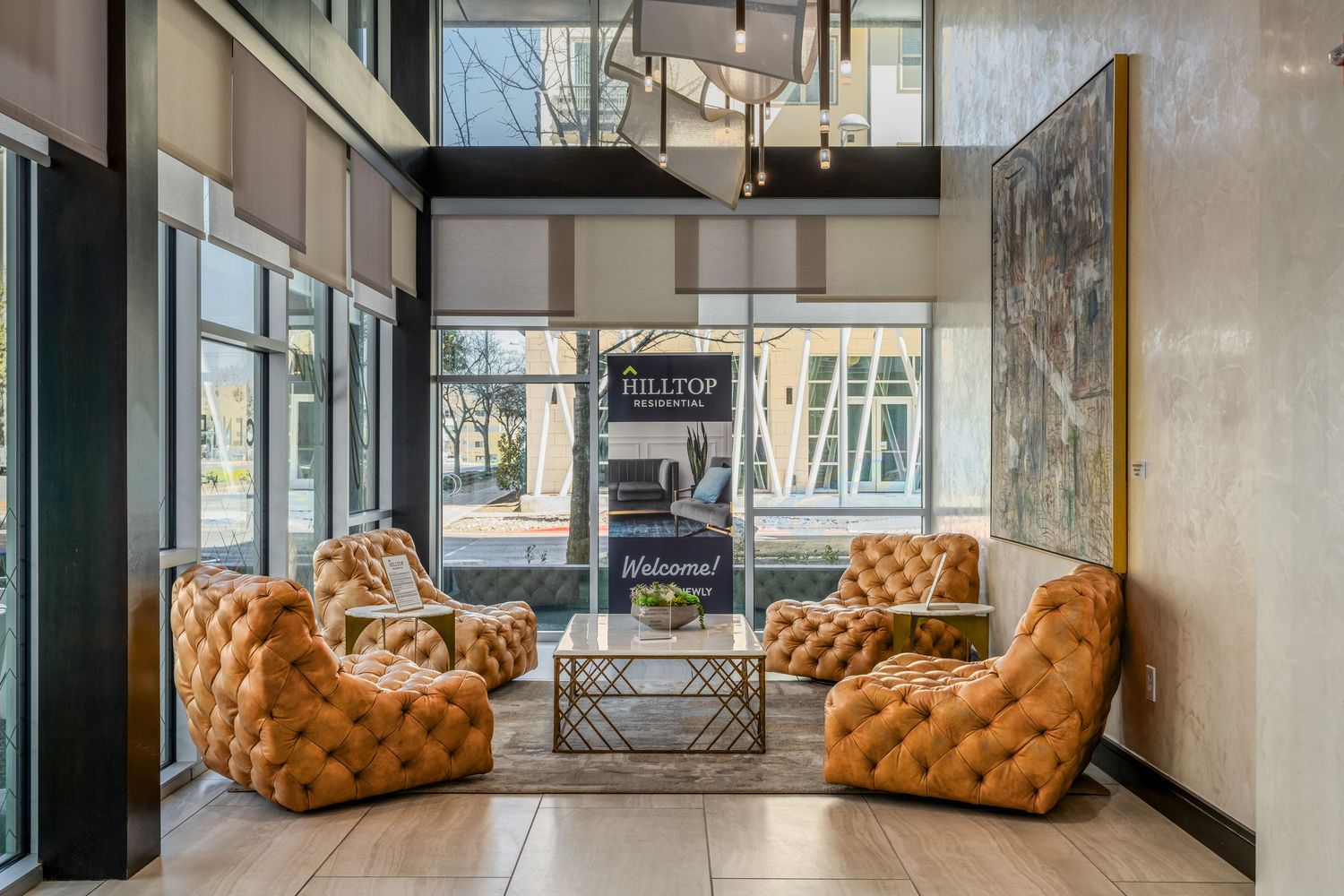 Elegant apartment lobby with tufted caramel leather chairs, gold coffee table, and large windows at Hilltop community.