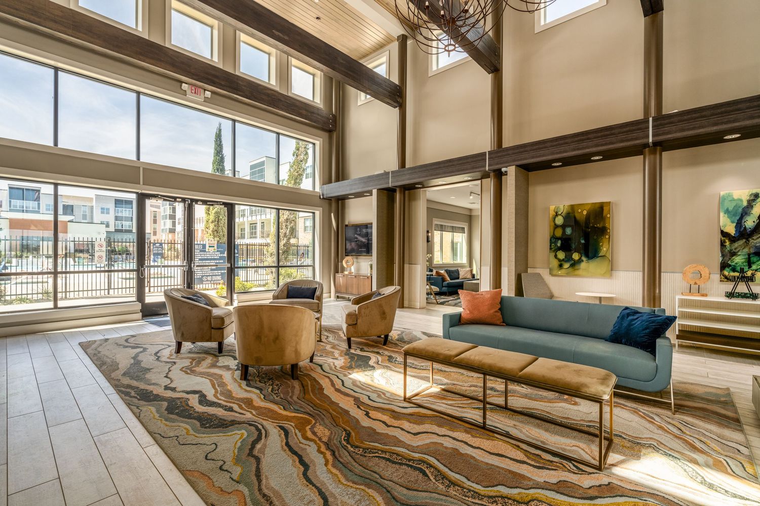 Spacious luxury apartment lobby with soaring ceilings, floor-to-ceiling windows, blue sofa, and vibrant swirl-patterned area rug.
