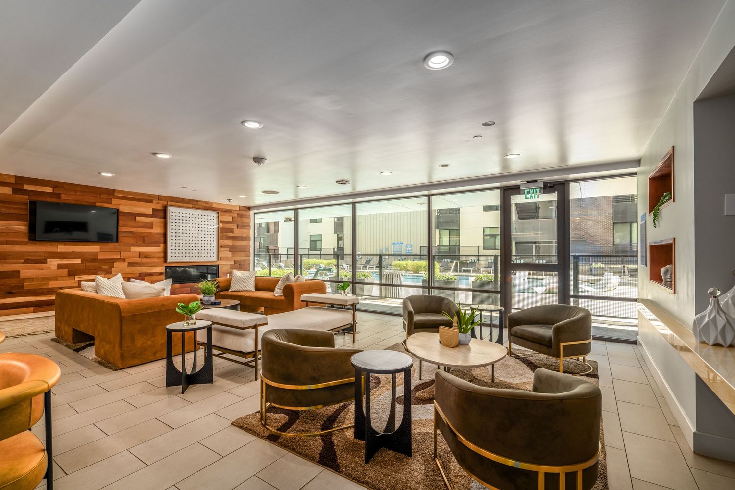 Modern apartment lounge with floor-to-ceiling windows, leather seating, wood accent wall, and city views.