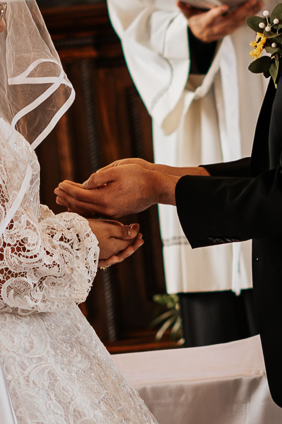 Bride and groom exchanging rings at altar during wedding ceremony, officiant in white robe visible in background.