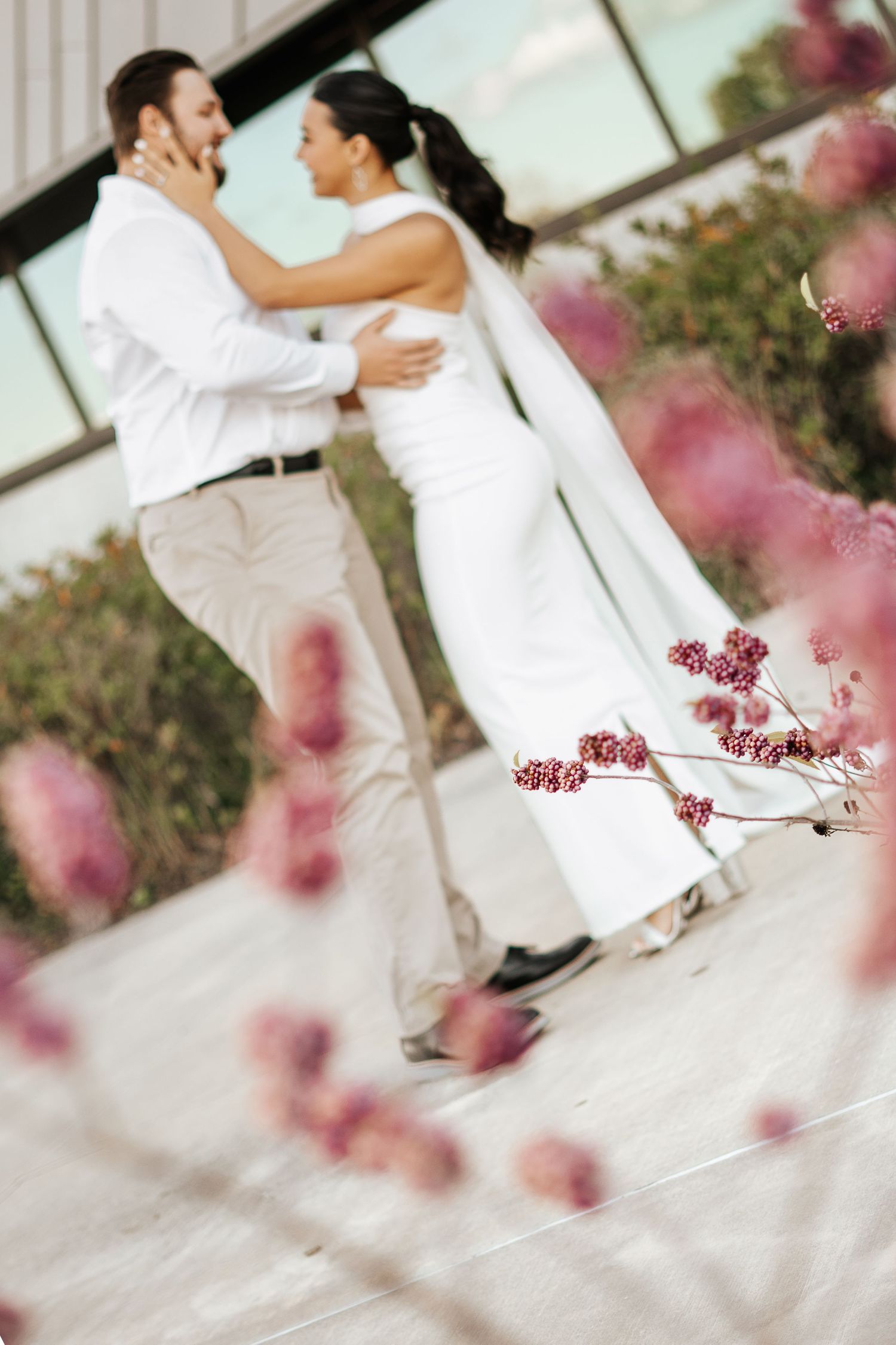Bride and groom sharing romantic embrace outdoors with pink flowering branches in the foreground.