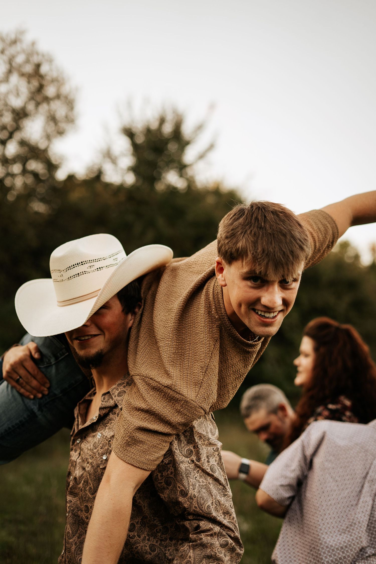 Young man giving piggyback ride to smiling boy in a candid outdoor family photo at sunset.