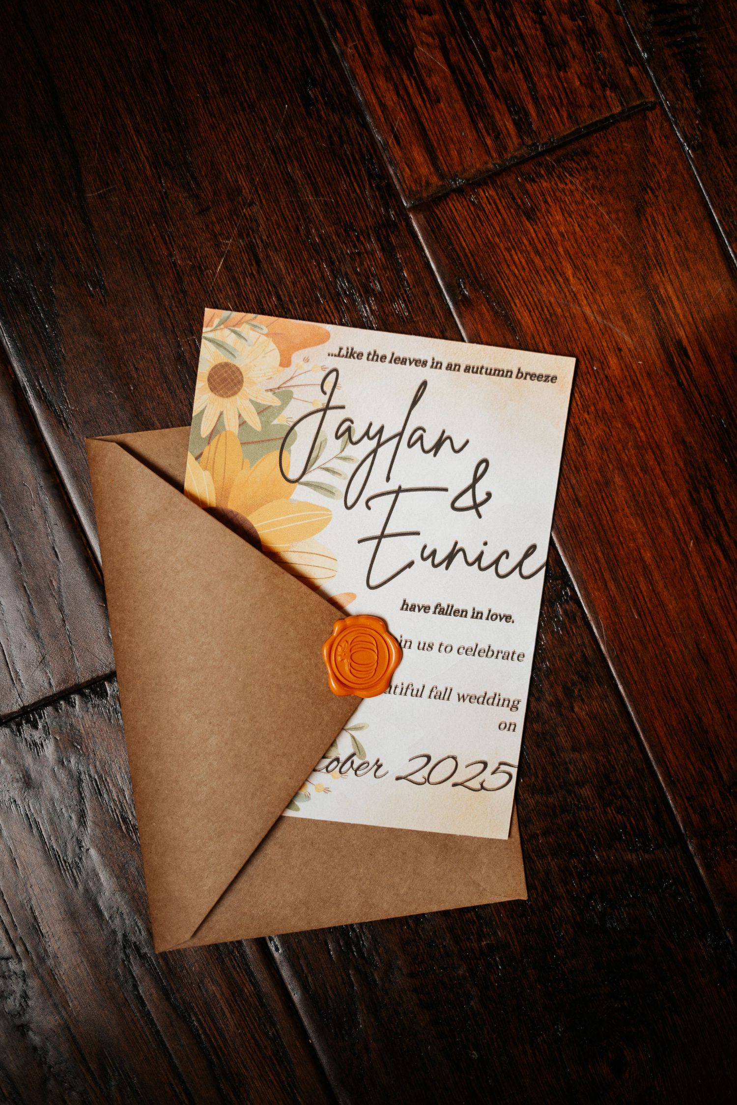 Elegant fall wedding invitation for Jaylan and Eunice with sunflower design, orange wax seal, and kraft envelope on wood.