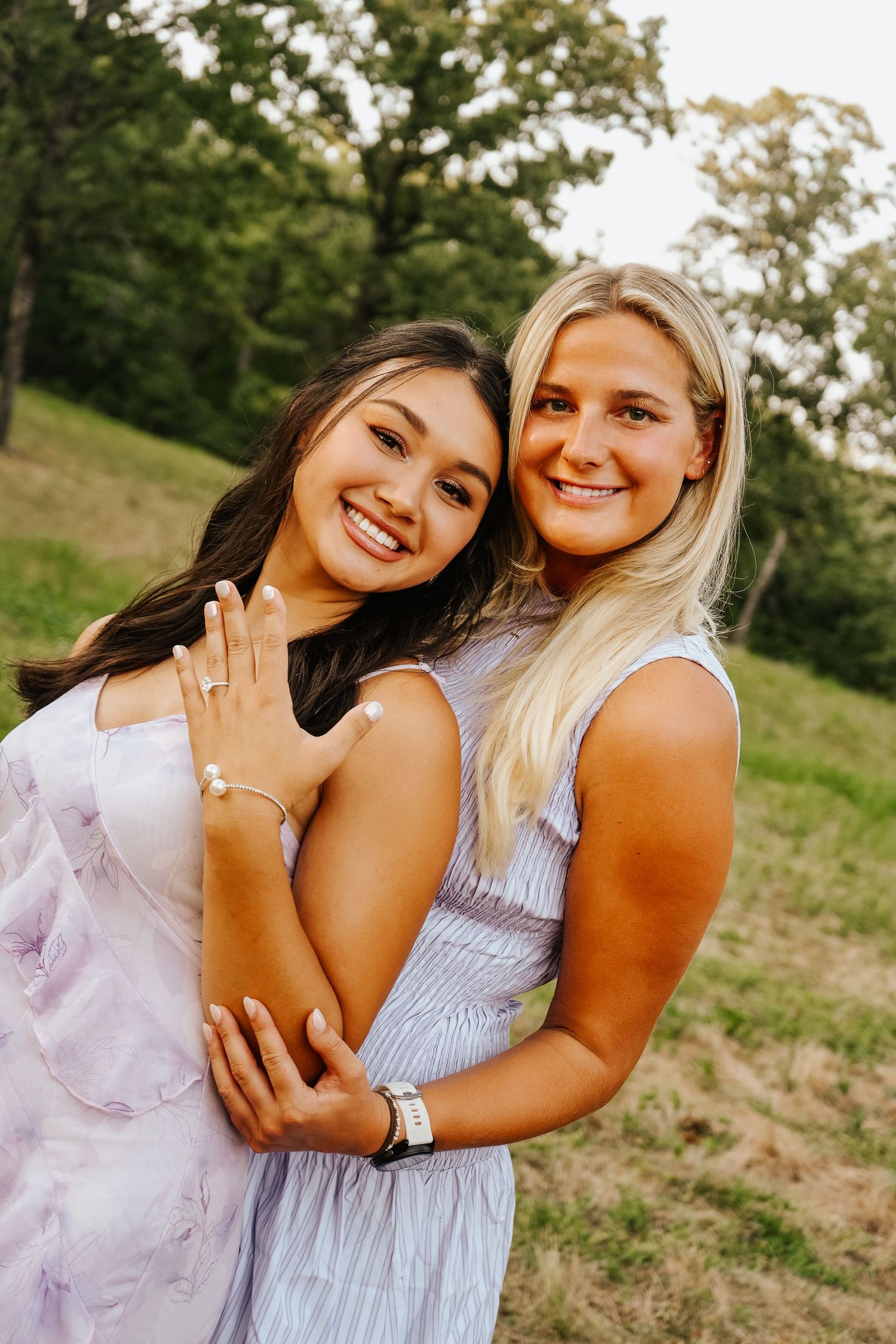Two smiling young women hugging outdoors, one showing off a bracelet on her wrist.