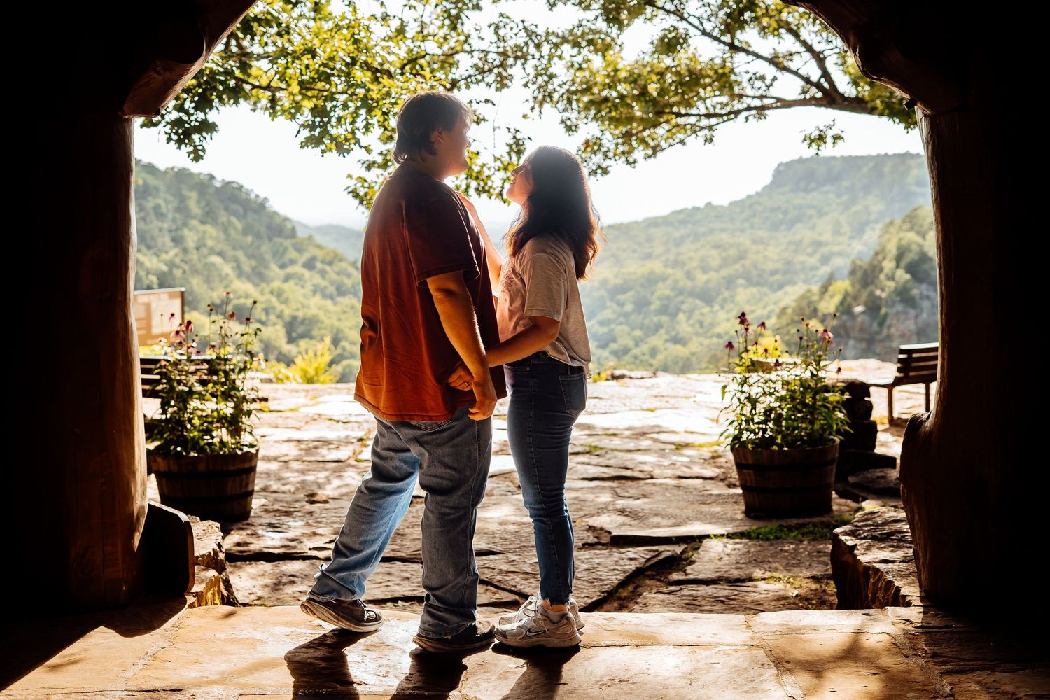 Romantic couple stands silhouetted in a stone archway overlooking a stunning mountain valley landscape.