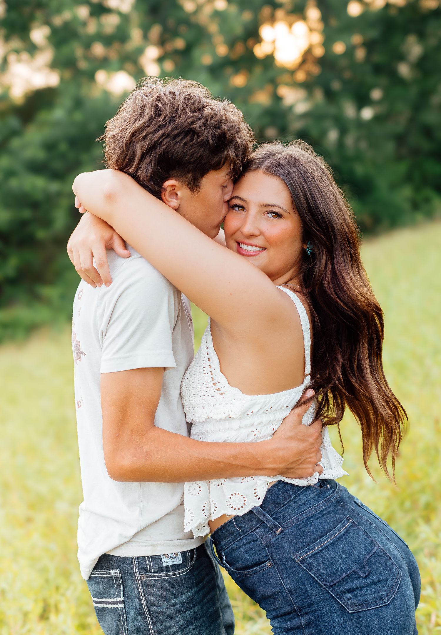 Happy brunette woman hugging her partner in a white tee in a sunlit green meadow.