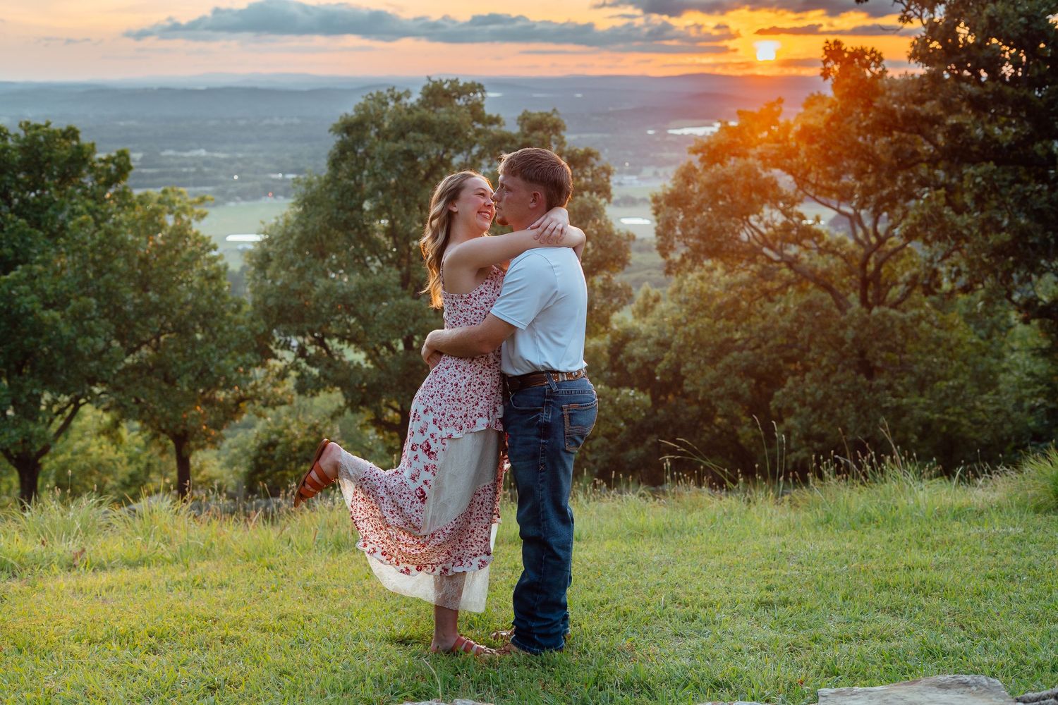 Couple embracing on a hilltop at sunset with a breathtaking golden sky and valley view behind them.