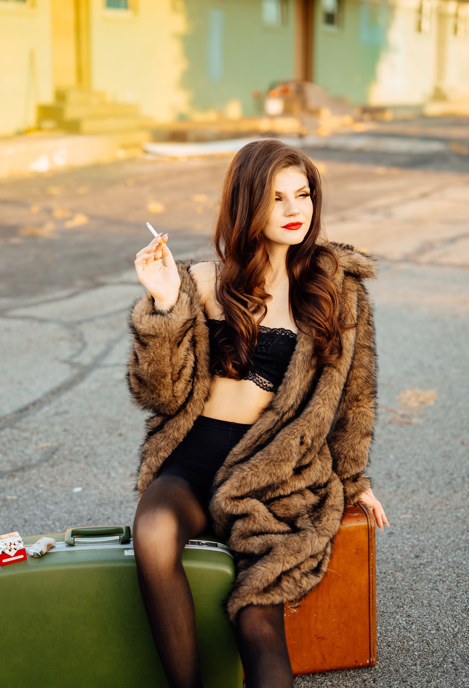 Glamorous woman in fur coat and black lingerie sitting on vintage suitcases smoking a cigarette.
