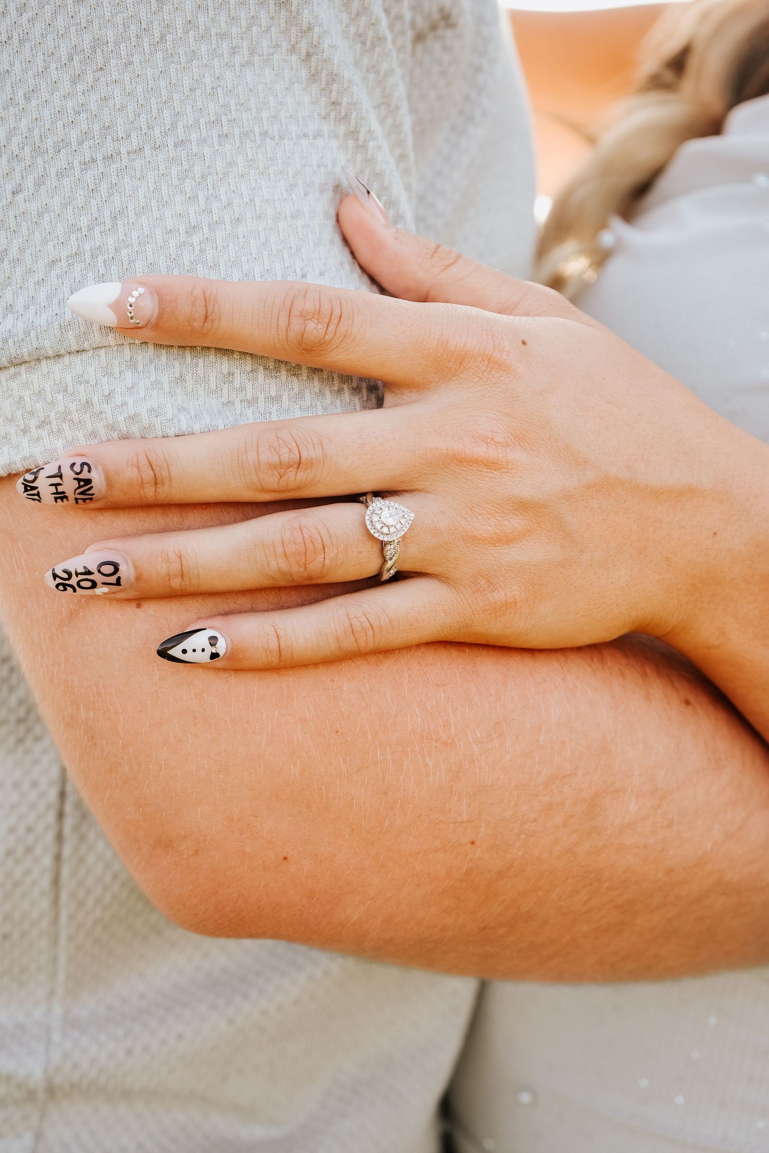 Close-up of womans hand with diamond engagement ring resting on partners arm with tattoos.