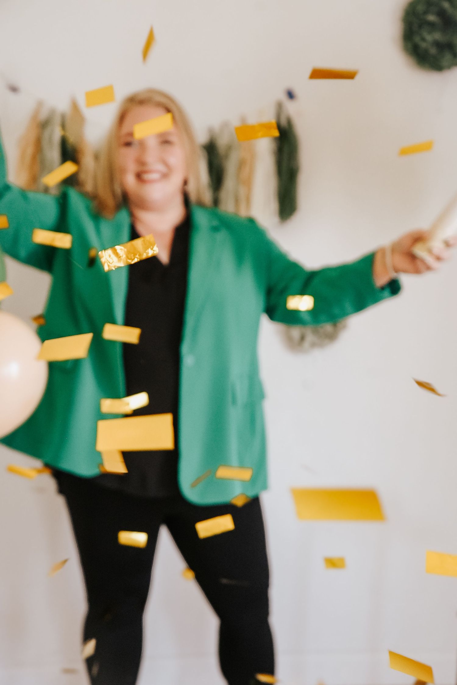 Joyful blonde woman in green blazer celebrating with gold confetti falling around her.