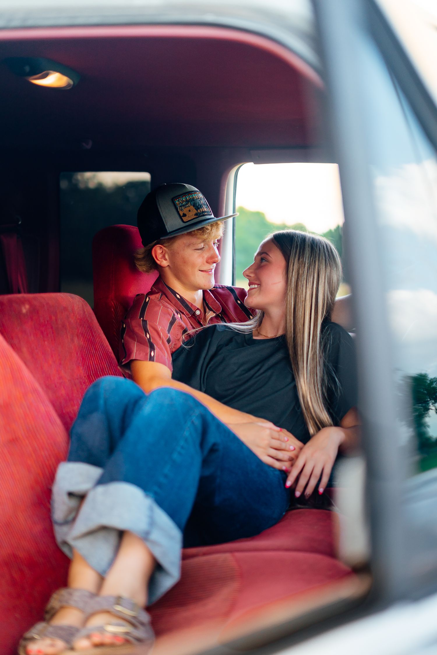 Couple cuddling and smiling at each other on red seats inside a classic truck cab.